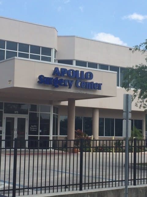 Entrance of Apollo Surgery Center in West Melbourne, Florida, a two-story medical facility with blue signage above the glass doors.