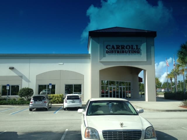 Exterior of the Carroll Distributing facility in Rockledge, Florida, a single-story commercial building with an arched glass entrance and parking in the foreground.