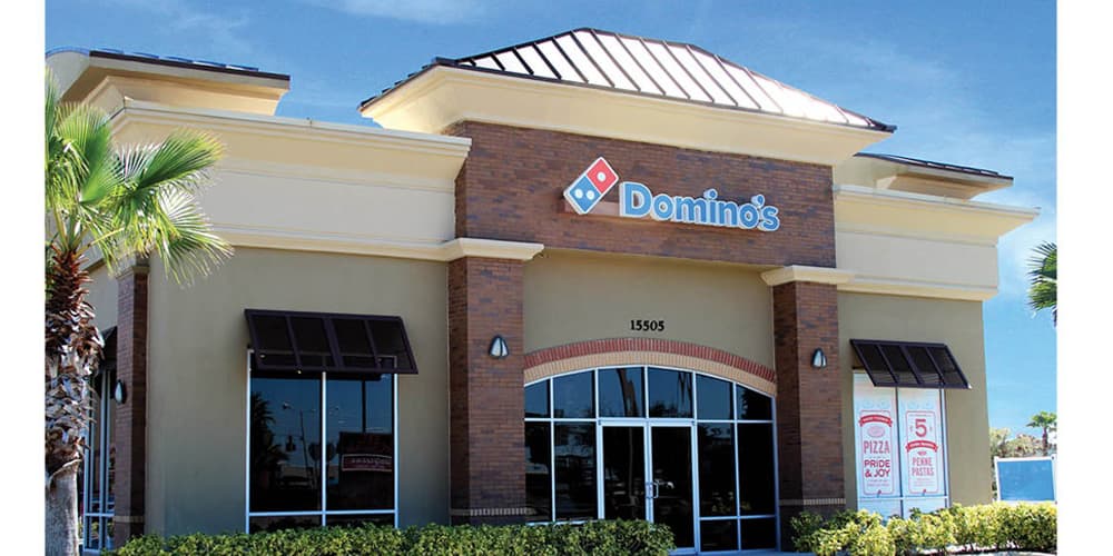 Exterior of the Domino's restaurant in Port Orange, Florida, a standalone storefront with brick accents, an arched glass entrance, and address 15505.