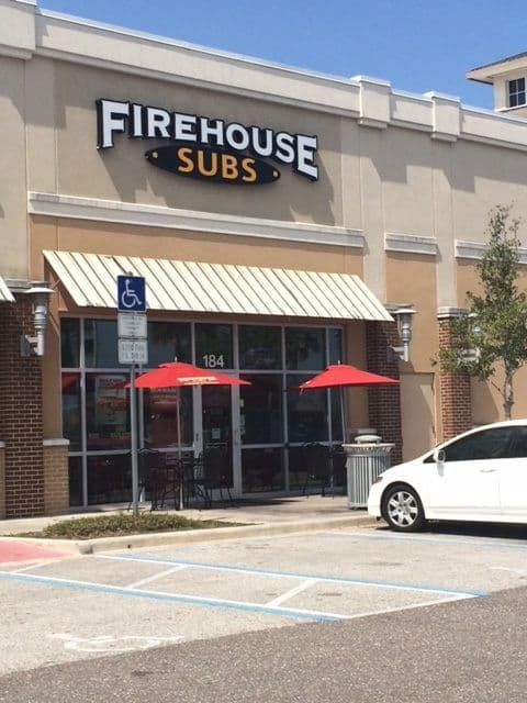 Storefront of Firehouse Subs unit 184 in West Melbourne, Florida, with outdoor seating, a striped awning, and an accessible parking space in front.