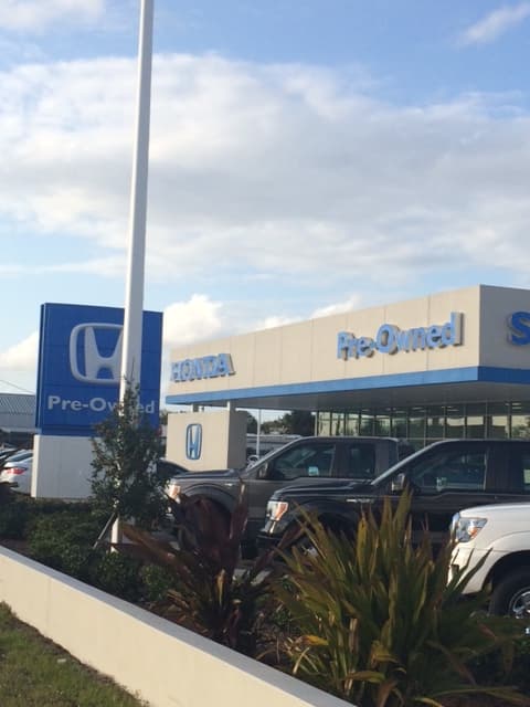 Exterior of the Honda of Palm Bay Pre-Owned building in Palm Bay, Florida, with Honda signage, showroom glass, and vehicles in the foreground.