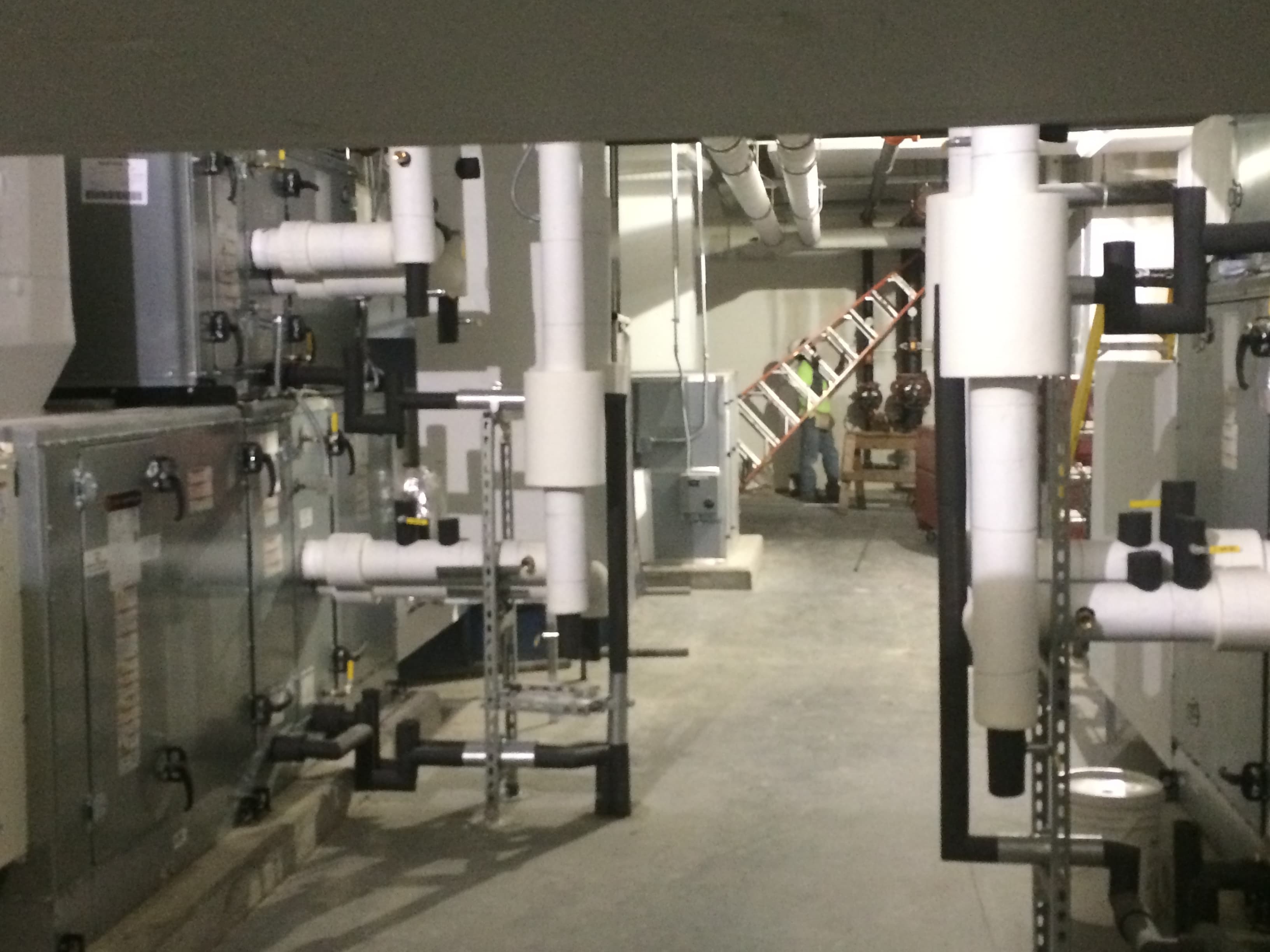 Mechanical room with air-handling equipment, insulated chilled-water piping, and strut-supported hydronic lines at Meadowlane Intermediate School in West Melbourne, Florida.