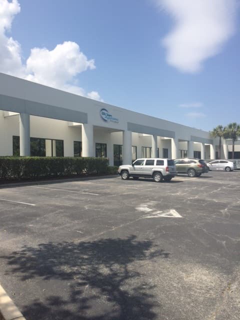 Exterior of the Vision Systems eyeglass assembly facility in West Melbourne, Florida, a single-story commercial building with a parking lot in the foreground.